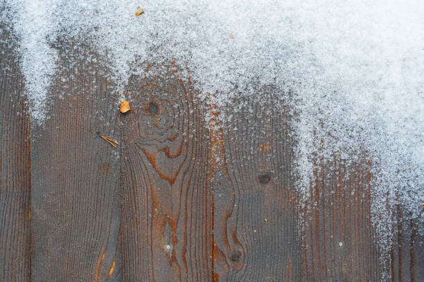 istock Dark floorboards are positioned vertically across the frame. The surface is partially covered with grains of white snow. There is a texture of treated pine wood. Background. Texture. Form. 1902825407