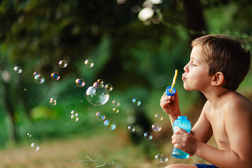 Side view of little boy blowing soap bubbles in nature