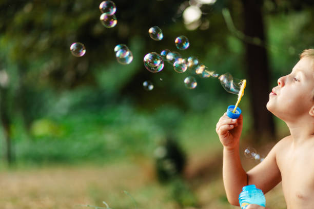 istock Side view of little boy blowing soap bubbles in nature 1902850455