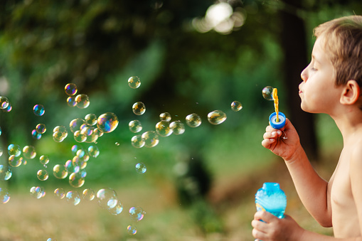 Side view of little boy blowing soap bubbles in nature