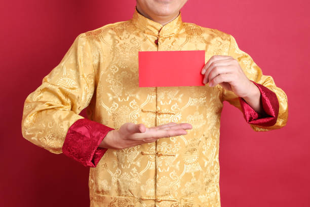 Happy Chinese new year. Asian Chinese energetic senior man wearing gold traditional cheongsam qipao or changshan dress with gesture of hand holding Chinese Red envelopes isolated on red background.