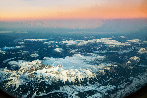 European Alps (Austrain) and orange horizont line of sunset  from window of airplane (Flying from   Georgia to German Bavaria) .. The distant valley is filled with fog and clouds