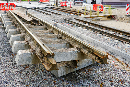 Old cut out tram track fragment with concrete sleepers, tram rails replacement in city street, red and white plastic barriers