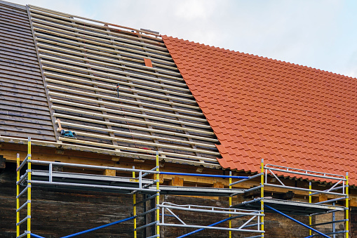 Installation of new red clay tiles on new wooden battens on the roof of a historic house, new covering of a tiled roof