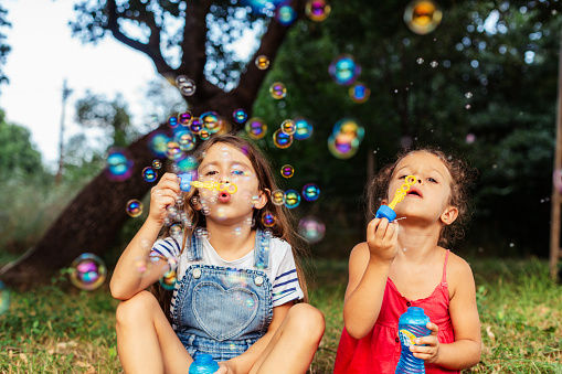 Two girls having fun blowing soap bubbles in nature