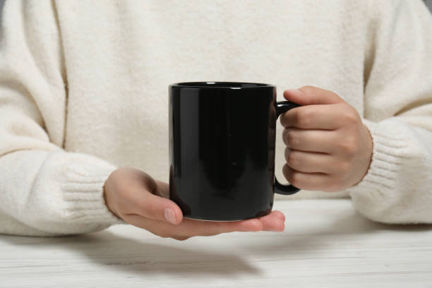 istock Woman holding black mug at white table, closeup. Mockup for design 1902953329