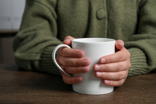 Woman holding white mug at wooden table, closeup