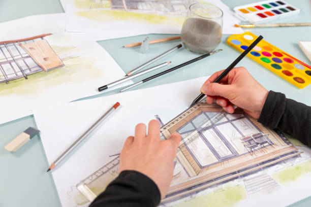 istock Architect illustrator working on hand drawn illustration of a modular house  using black pencil to draw lines on a sketch. 1902983366
