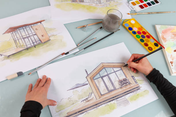 istock Architect illustrator working on hand drawn illustration of a modular house  using black pencil to draw lines on a sketch. 1902983369