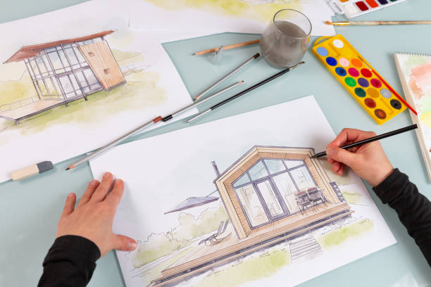 istock Architect illustrator working on hand drawn illustration of a modular house  using black pencil to draw lines on a sketch. 1902983370