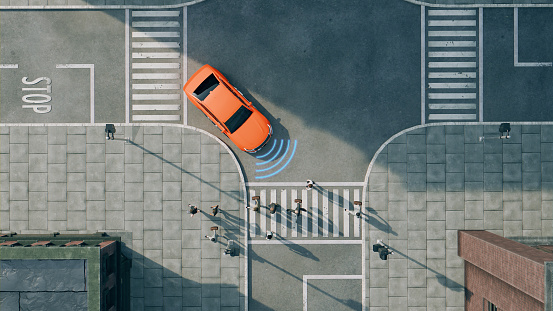 Aerial view of a bright orange car driving on a street. The car is next to a pedestrian crossing and in front of a stop line with the word 
