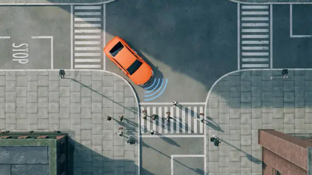 Aerial view of a bright orange car driving on a street. The car is next to a pedestrian crossing and in front of a stop line with the word "Stop" painted on the road. The car uses sensors and radar to detect the pedestrians. Concept of new car technology like autonomous driving.