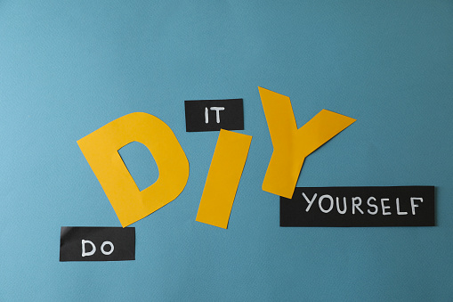 Phrase Do It Yourself and abbreviation DIY made of letters on light blue background, flat lay