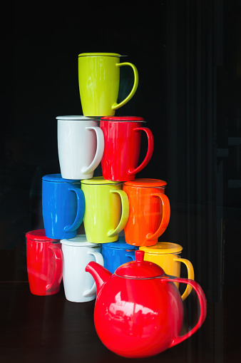 A colorful stack of ceramic tea mugs with a bright red teapot in a shop window.