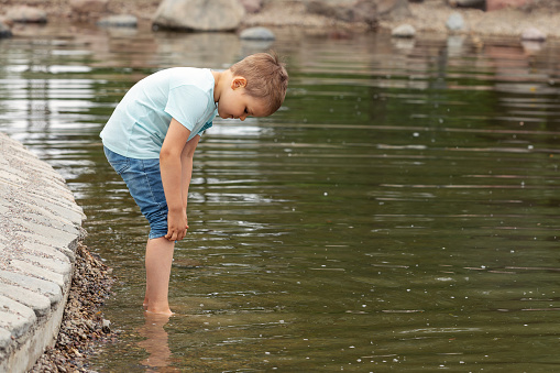 A little boy raises his jeans so that he can wade into the water and not get wet.