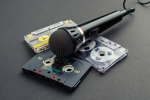 A nostalgic look reminiscent of 80's karaoke house parties with a microphone and three audio cassettes for recording. Black paper background, photo toned.