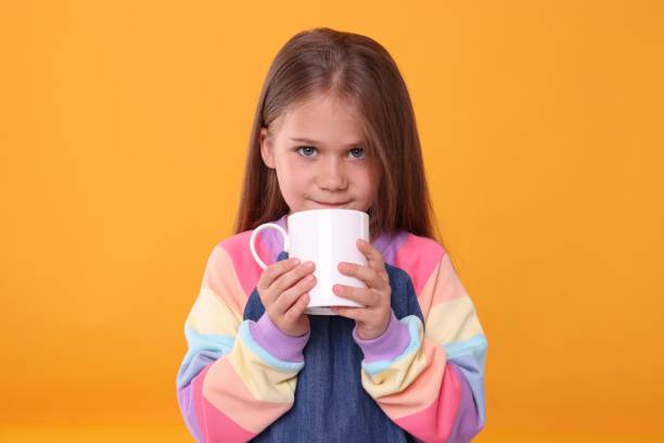 istock Cute girl drinking beverage from white ceramic mug on orange background 1903022865