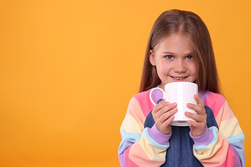 Happy girl with white ceramic mug on orange background, space for text