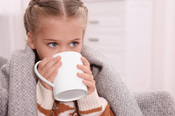 istock Cute girl under plaid drinking beverage from white ceramic mug at home, space for text 1903025450