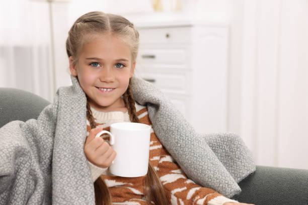 istock Happy girl under plaid with white ceramic mug on sofa at home, space for text 1903025634