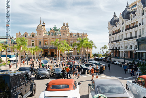 Monaco, Monte-Carlo, 29 September 2022 - Square Casino Monte-Carlo at sunny day, luxury cars, famous Hotel de Paris, wealth life, tourists take pictures of the landmark, pine trees, flowers. High quality photo