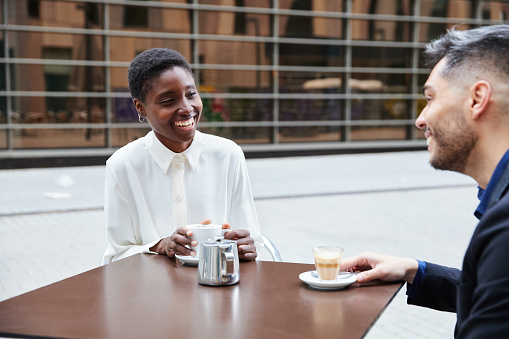 African businesswoman sitting drinking coffee with her colleague. They are laughing while enjoying their free time.