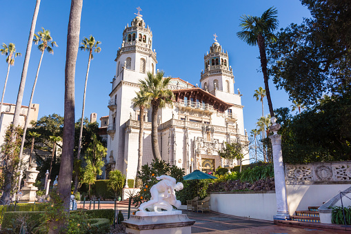 Hearst Castle, San Simeon, California - USA: Hearst Castle from the front showing full facade, towers, palm trees, sun, clear blue sky