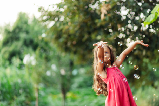 Little girl having fun catching soap bubbles in the yard