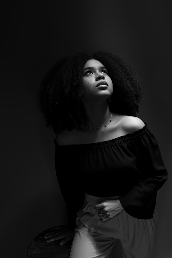 Black and white portrait of young woman with black power hair looking up. Isolated on blue background.
