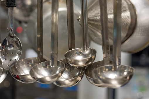 Stainless steel cooking utensils hanging in a commercial industrial kitchen.