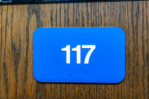 Blue 117 sign with braille, on a wooden door