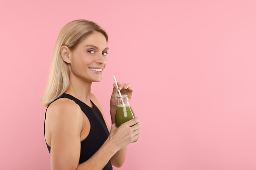 Happy woman with glass bottle of fresh celery juice on pink background. Space for text