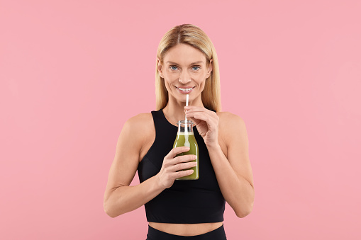 Happy woman with glass bottle of fresh celery juice on pink background