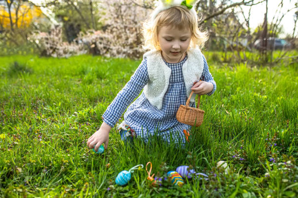 istock easter eggs hunt. Little girl with baskets in hands gathering colorful egg in park. 1903163371