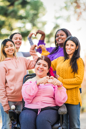 Women friendship together with a person on wheelchair cause cerebral palsy. Multicultural happy feminist gesture for inclusion, cooperation and sorority