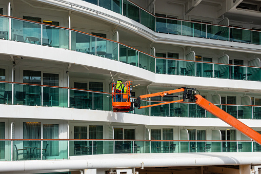 Vancouver, Canada - 10th September 2024: Two workmen on an Engine Powered Boom Lift painting the balcony ceilings of a large cruise ship which is docked at the Port of Vancouver between cruises. Canada Place, Vancouver, Canada.