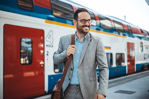 Photo of a smiling businessman at train station.  Confident professional is wearing suit. He is standing at railroad station platform. Businessman at the Train Station