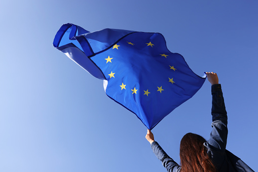 Woman holding European Union flag against blue sky outdoors, low angle view