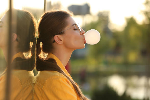 istock Beautiful young woman in glasses blowing bubble gum outdoors. Space for text 1903215904