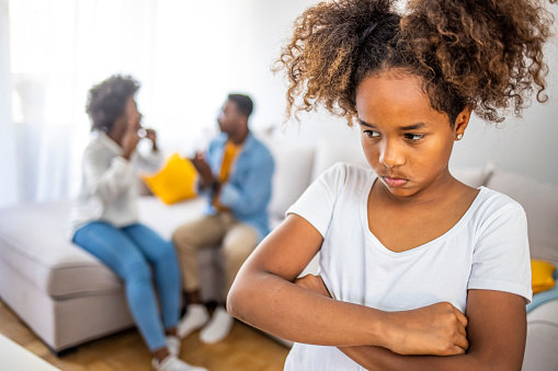 Sad little girl is looking at camera while her parents are arguing in the background. Rising family problems hurt children's minds. Stop violence in children Help prevent abuse and bring him back to family.