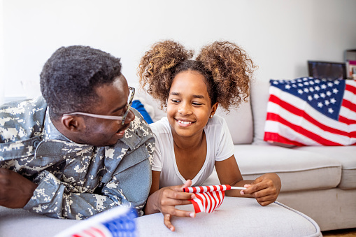 Photo of American soldier playing with his daughter at home. Mid adult African American military soldier is happy to see his preschool age daughter. He has just returned from overseas assignment.