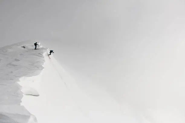 Great view of freeriders on splitboard riding down from top of ridge. Ski touring in mountains.