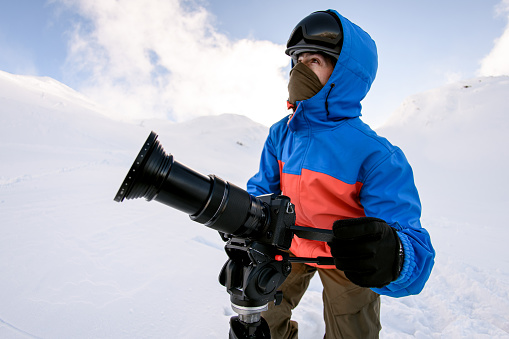 view on man photographer outdoor with camera on snowy mountain. Snow and winter activities, skitouring in mountains.