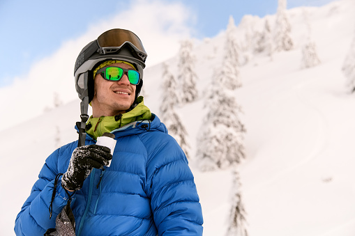 portrait of young smiling man in ski goggles against the background of snow-capped mountains. Ski touring concept