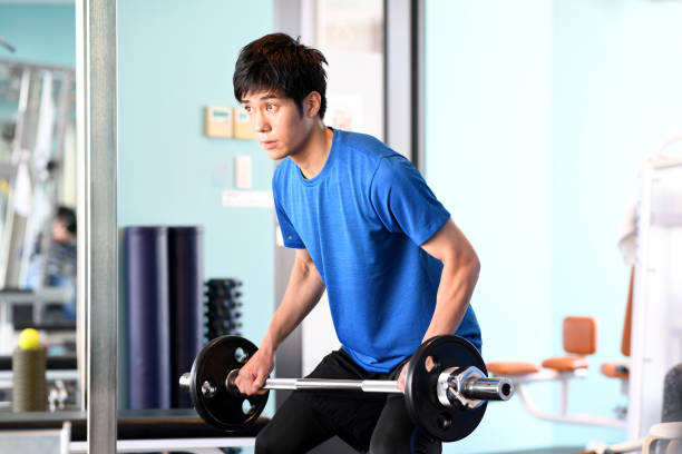istock Young Asian man doing strength training while holding a barbell at the gym 1903311223