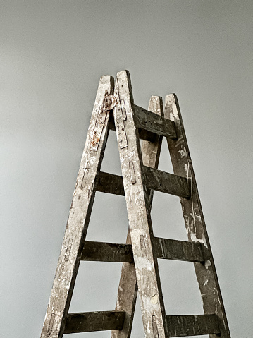 A paint-splattered ladder used for building maintenance is standing in a room with a plain background wall.