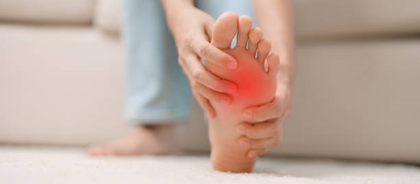 woman having barefoot pain during sitting on couch at home. foot ache due to plantar fasciitis and waking longtime. health and medical concept - longtime foto e immagini stock