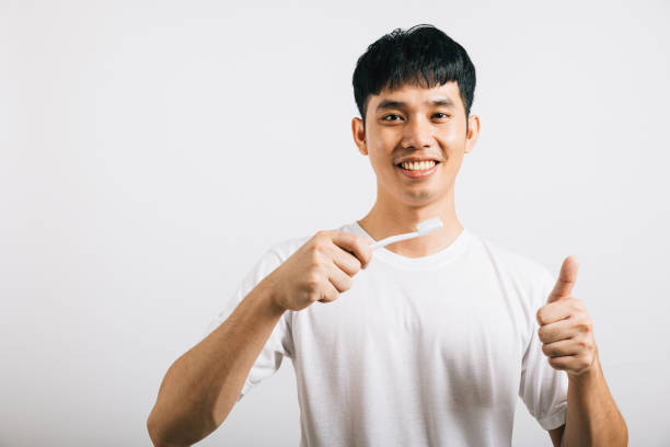 Jovem asiático sorridente demonstra escovação dentária adequada e aprovação para a saúde dental - foto de acervo