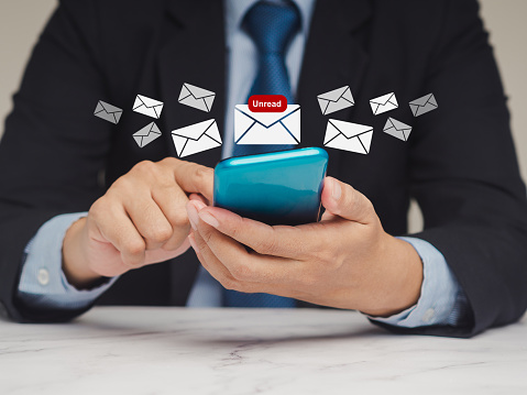 Businessman in a suit using a smartphone receives a new message with email icons while sitting at the table. Email notification on a mobile phone. Email marketing concept. Close-up photo