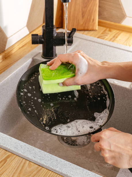 istock a girl washes a frying pan with a dish sponge 1903611114